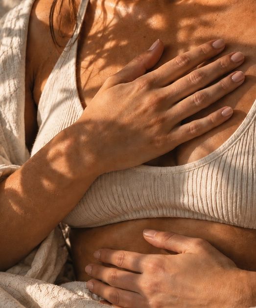 Una persona con las manos sobre el pecho y el abdomen, entre luz y sombras de hojas