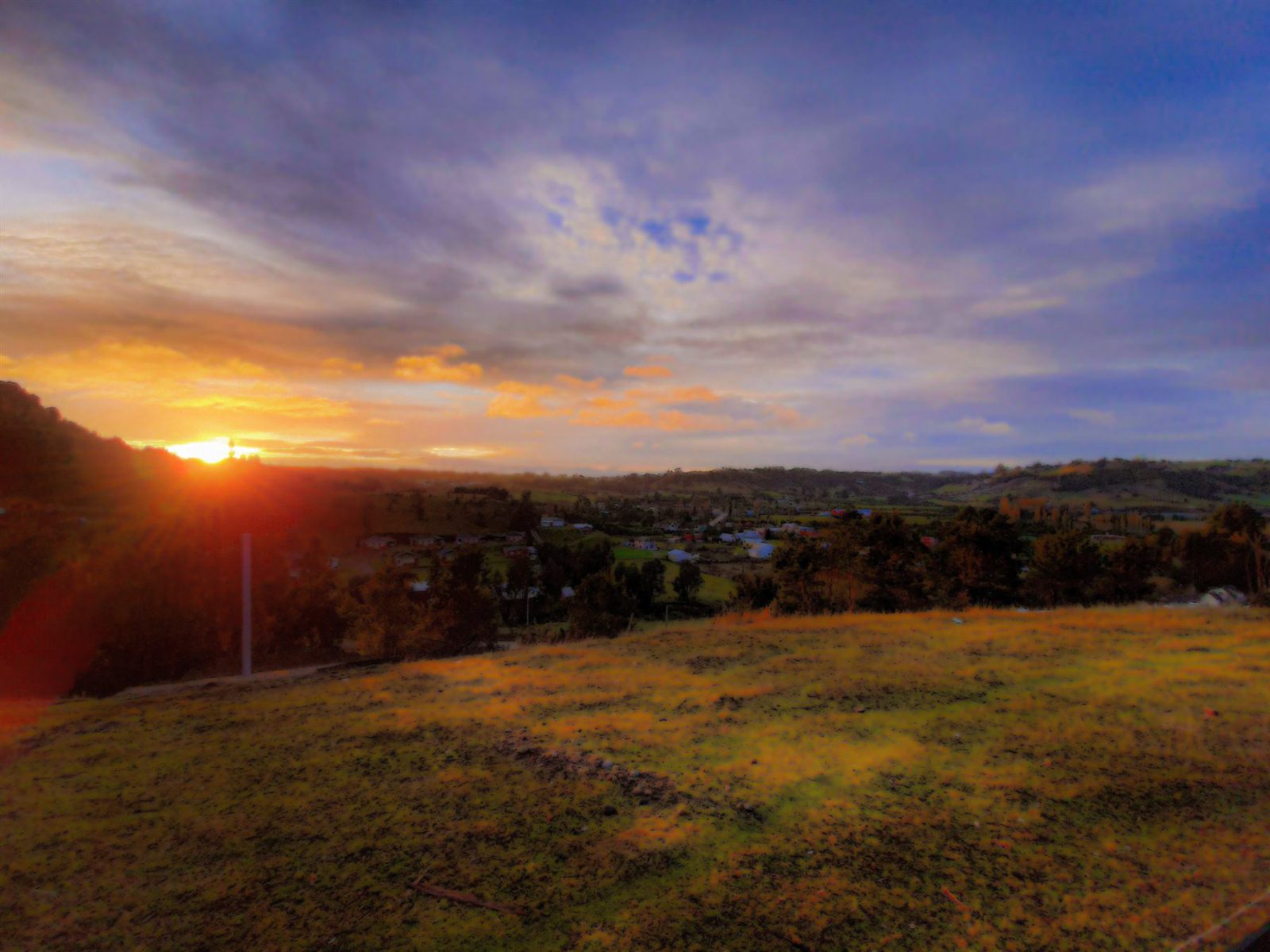 Atardecer sobre un valle, con el sol asomando entre las colinas